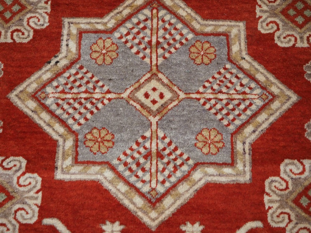 An antique East Turkestan Khotan wool area rug featuring three light blue geometric star medallions on a red field within wide cream and beige patterned borders. View XI