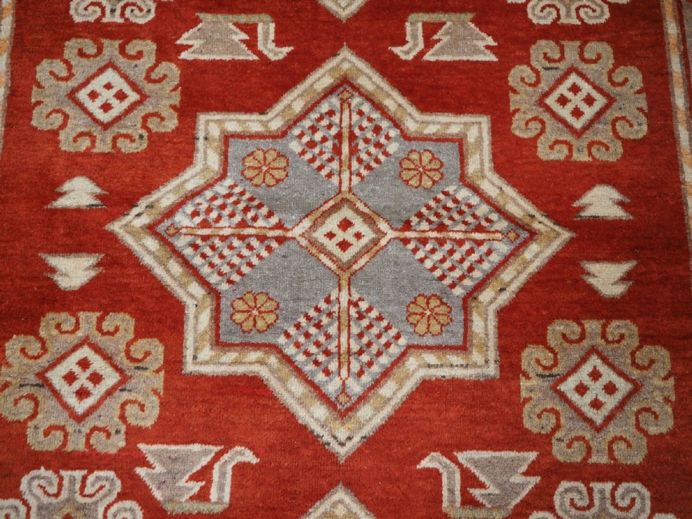 An antique East Turkestan Khotan wool area rug featuring three light blue geometric star medallions on a red field within wide cream and beige patterned borders. View XIII