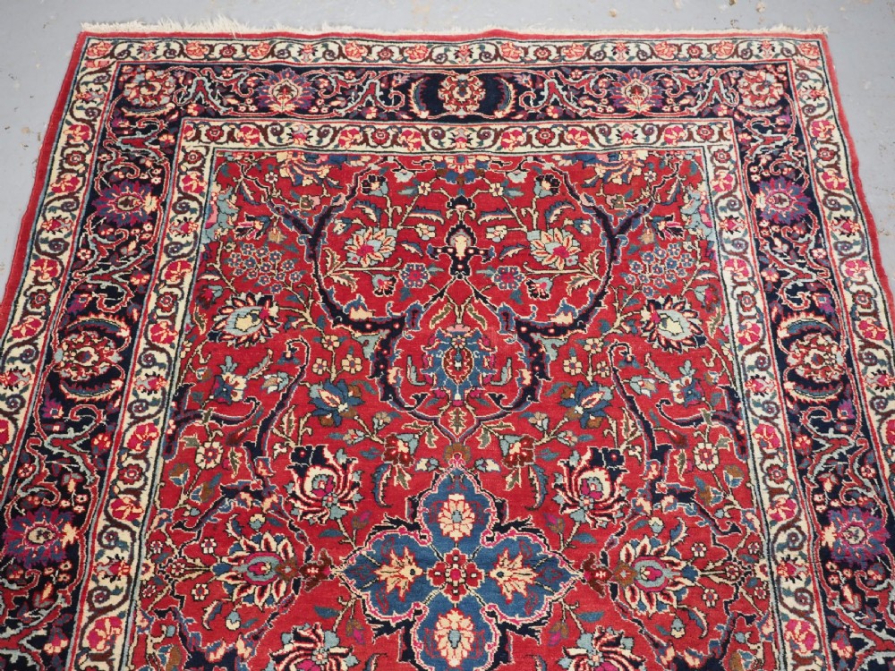A hand-knotted Tabriz wool rug featuring a blue central star medallion surrounded by floral scrollwork in red, cream, and navy blue with an ornate border. View III