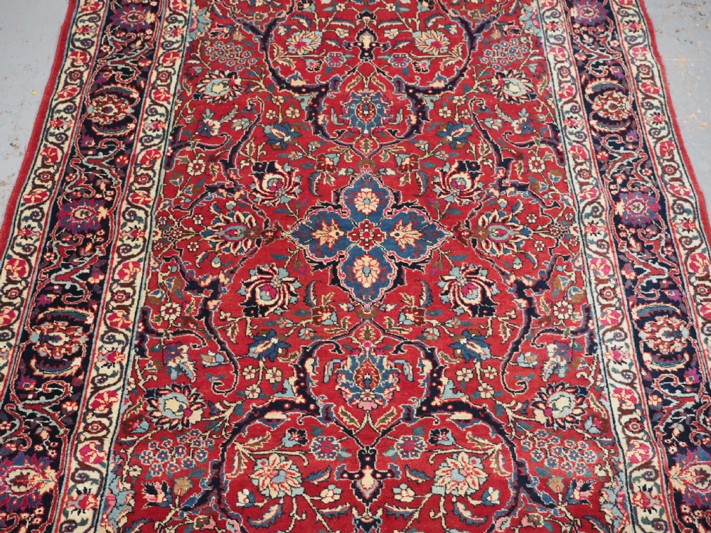 A hand-knotted Tabriz wool rug featuring a blue central star medallion surrounded by floral scrollwork in red, cream, and navy blue with an ornate border. View IV