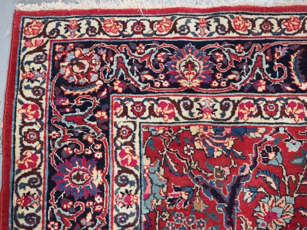 A hand-knotted Tabriz wool rug featuring a blue central star medallion surrounded by floral scrollwork in red, cream, and navy blue with an ornate border. View V