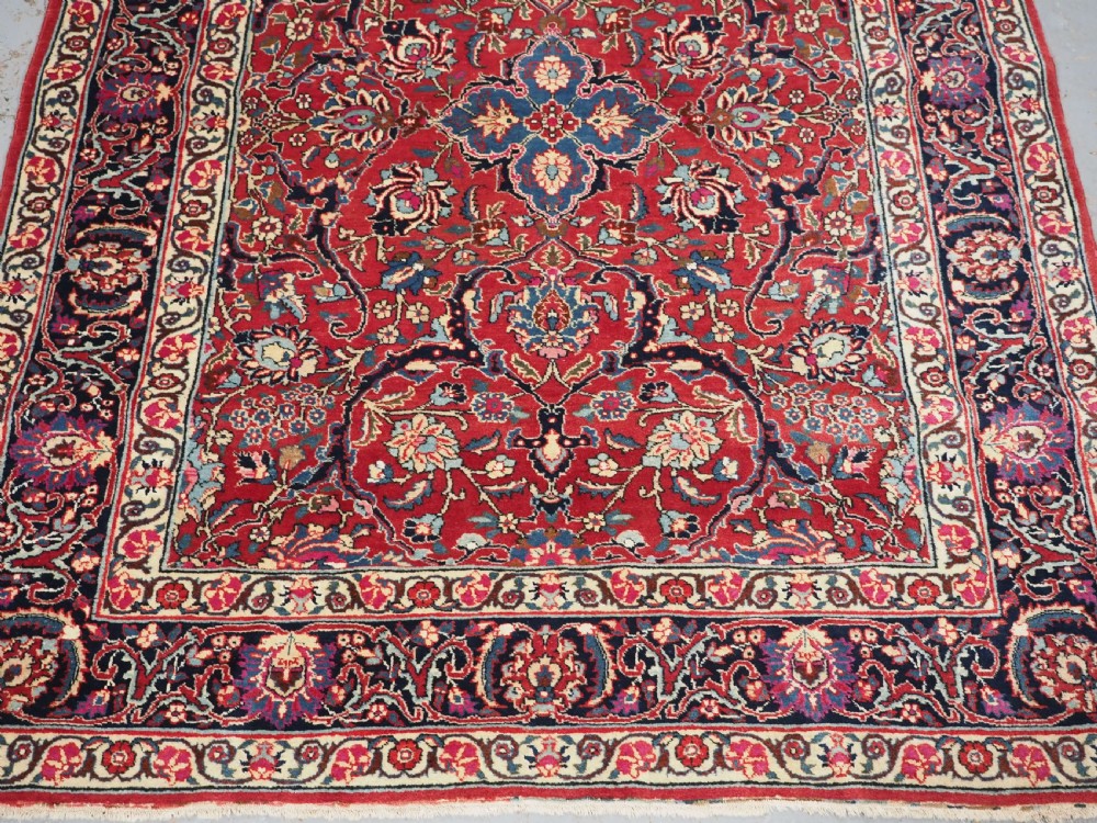 A hand-knotted Tabriz wool rug featuring a blue central star medallion surrounded by floral scrollwork in red, cream, and navy blue with an ornate border. View VI