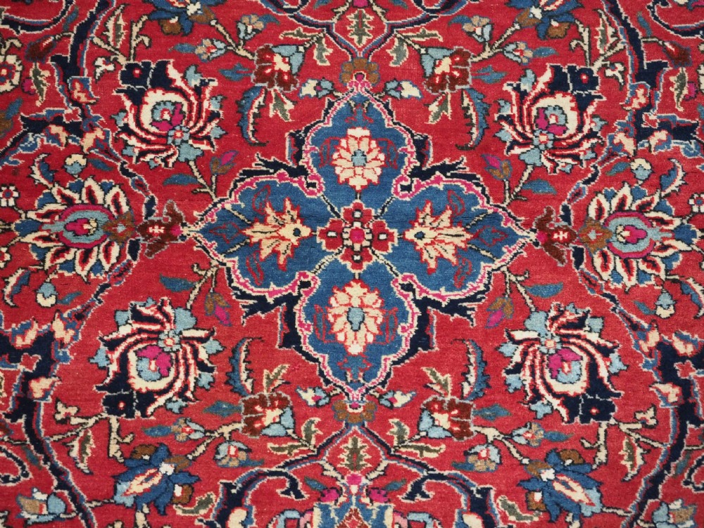 A hand-knotted Tabriz wool rug featuring a blue central star medallion surrounded by floral scrollwork in red, cream, and navy blue with an ornate border. View IX
