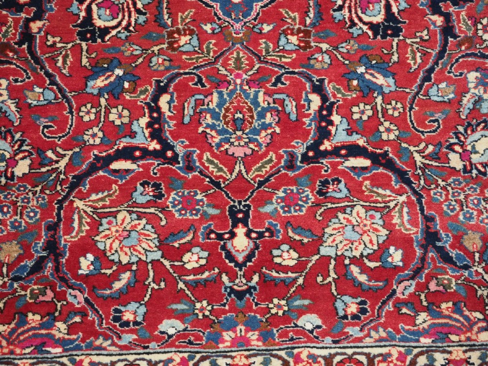 A hand-knotted Tabriz wool rug featuring a blue central star medallion surrounded by floral scrollwork in red, cream, and navy blue with an ornate border. View X
