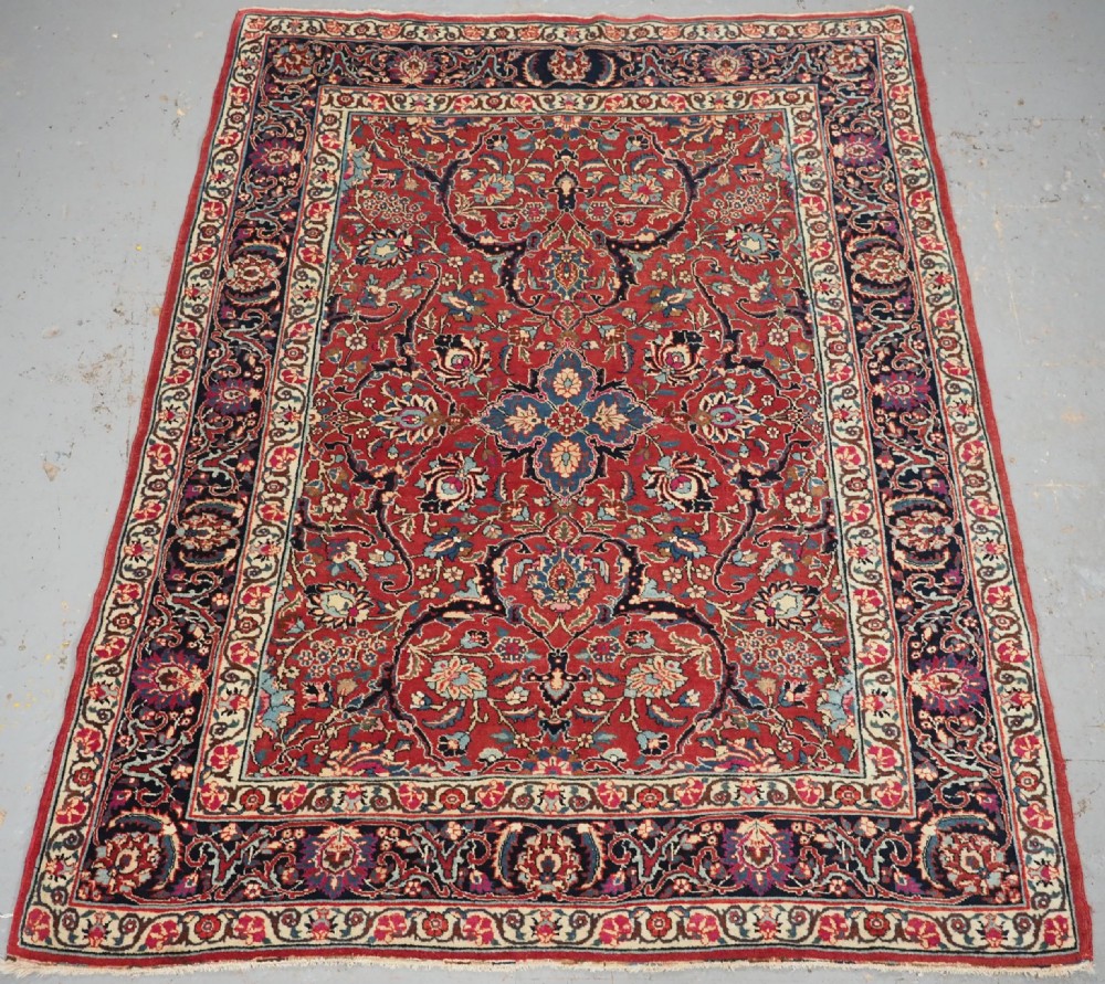 An antique hand-knotted Persian Tabriz wool rug featuring a dark navy central medallion surrounded by a red floral field and decorative navy borders.