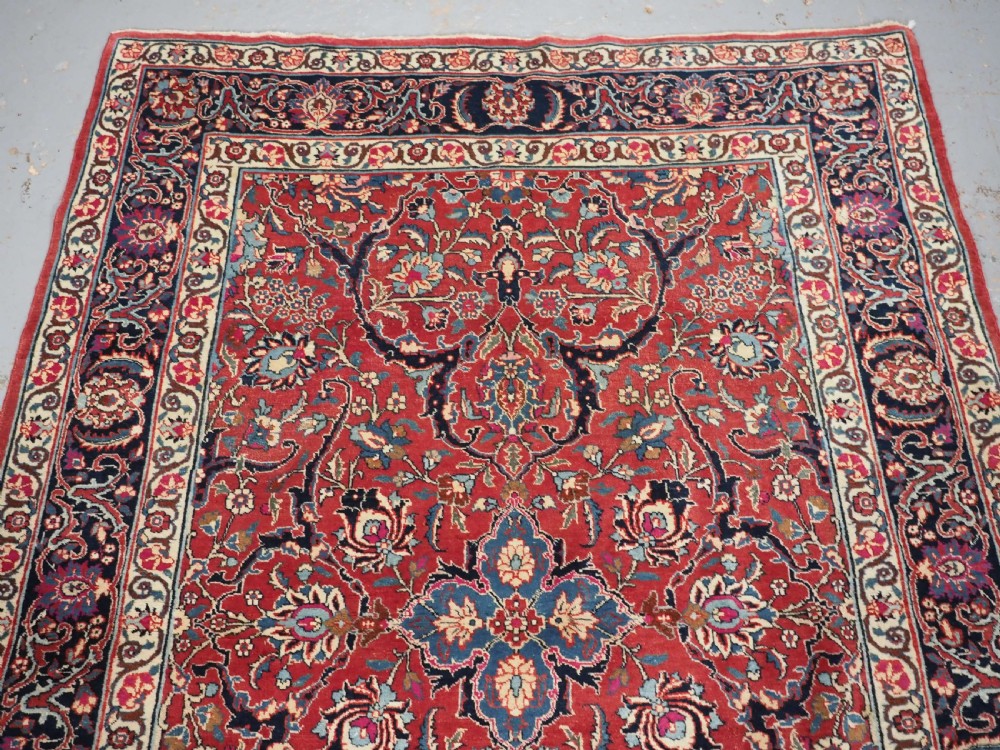 An antique hand-knotted Persian Tabriz wool rug featuring a dark navy central medallion surrounded by a red floral field and decorative navy borders. View III