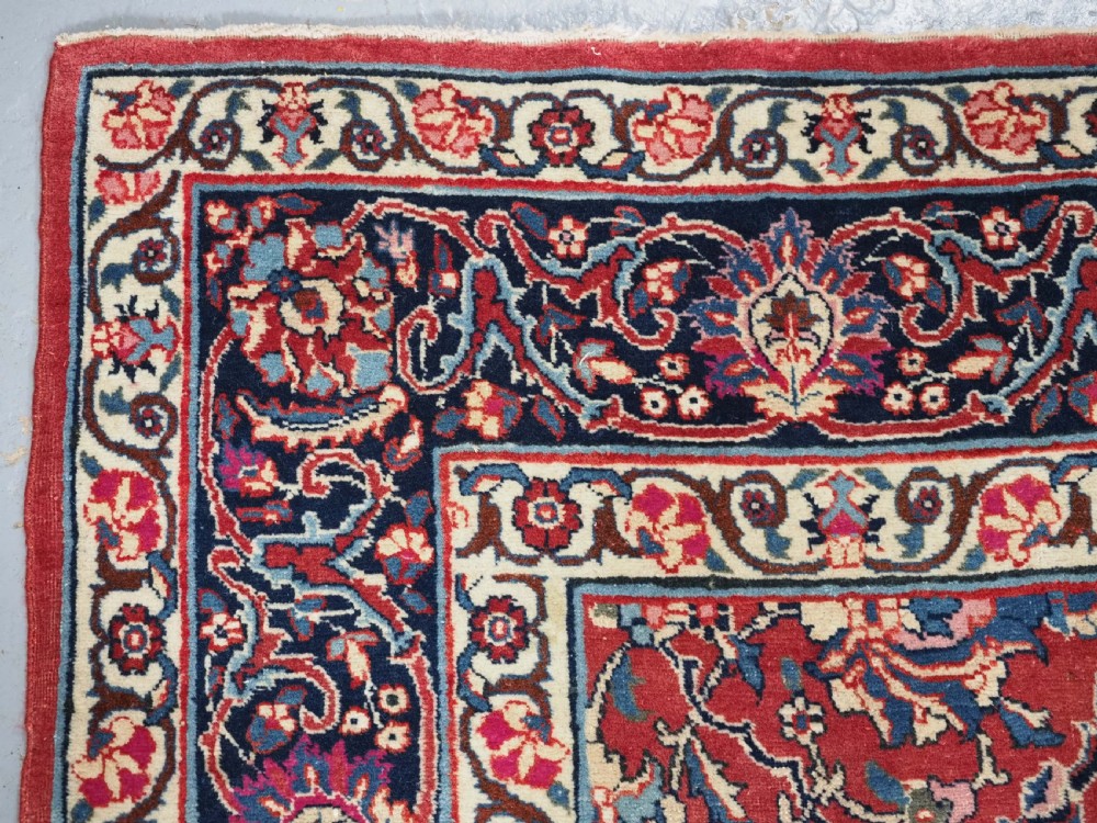 An antique hand-knotted Persian Tabriz wool rug featuring a dark navy central medallion surrounded by a red floral field and decorative navy borders. View IV