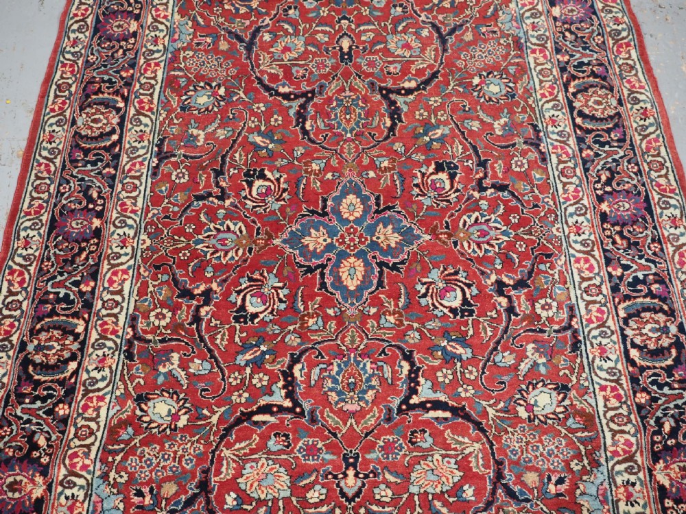 An antique hand-knotted Persian Tabriz wool rug featuring a dark navy central medallion surrounded by a red floral field and decorative navy borders. View V