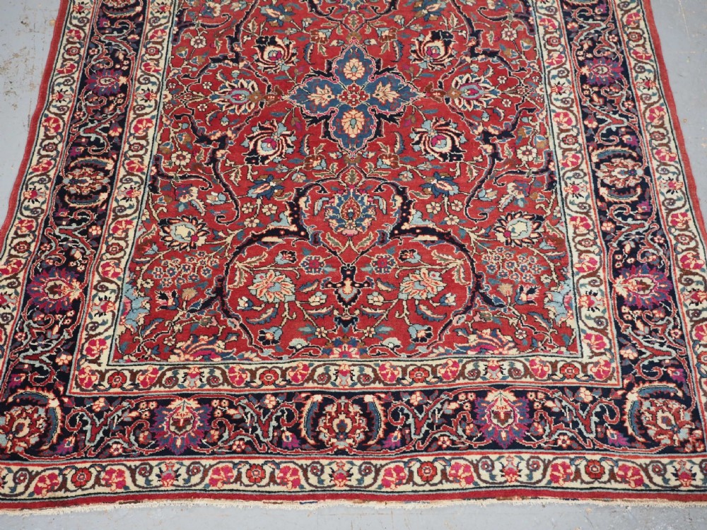 An antique hand-knotted Persian Tabriz wool rug featuring a dark navy central medallion surrounded by a red floral field and decorative navy borders. View VI