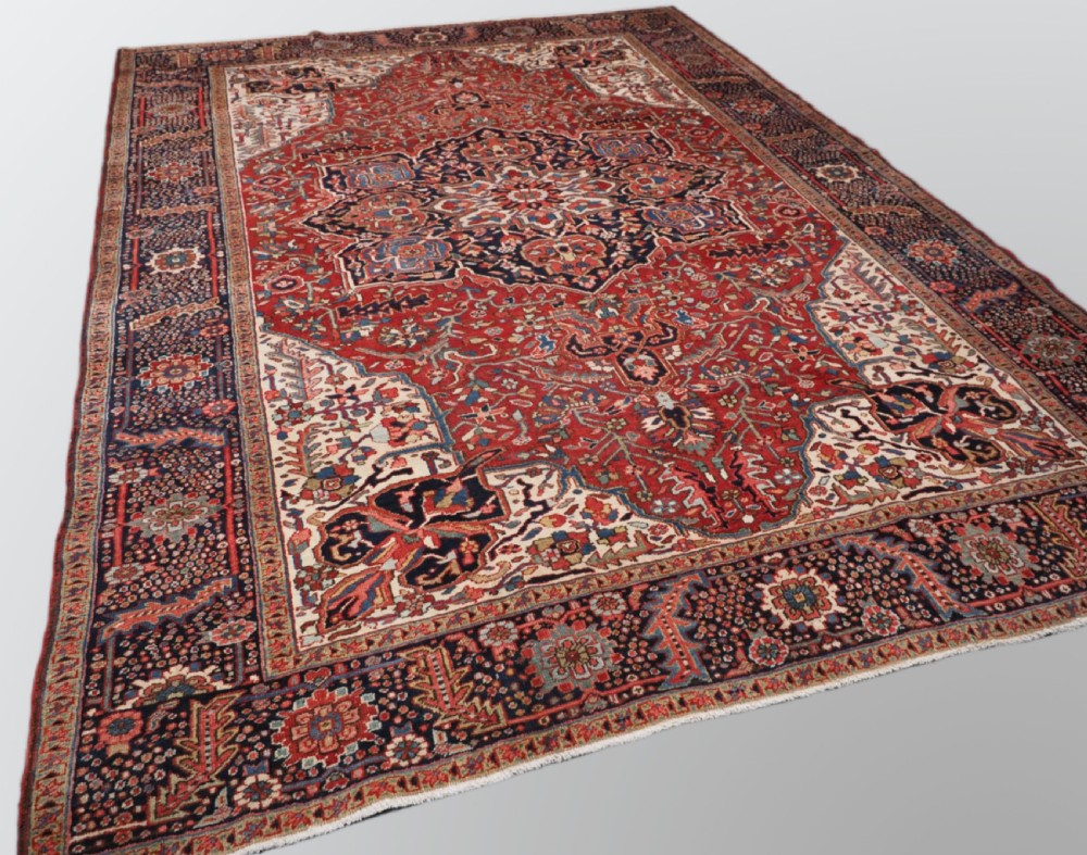 An antique hand-knotted Persian Heriz rug featuring a large geometric central medallion in navy blue, set upon a red field with off-white corner spandrels and a wide decorative border. View II