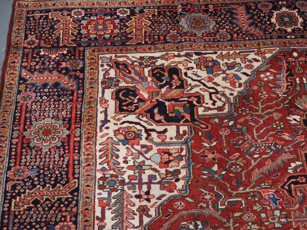 An antique hand-knotted Persian Heriz rug featuring a large geometric central medallion in navy blue, set upon a red field with off-white corner spandrels and a wide decorative border. View VIII