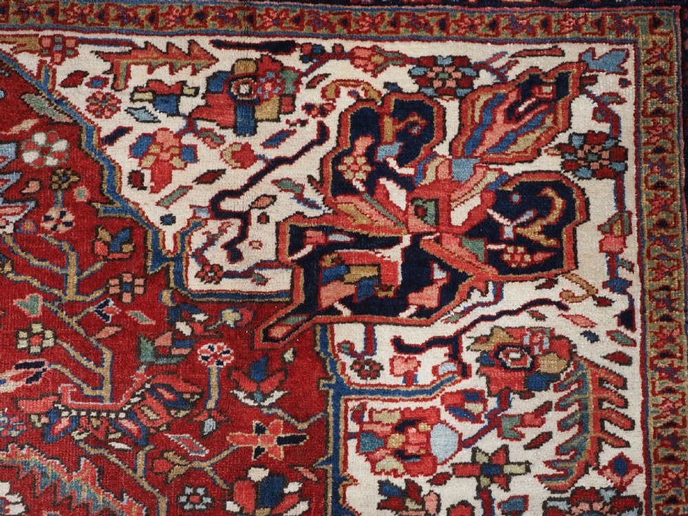 An antique hand-knotted Persian Heriz rug featuring a large geometric central medallion in navy blue, set upon a red field with off-white corner spandrels and a wide decorative border. View X