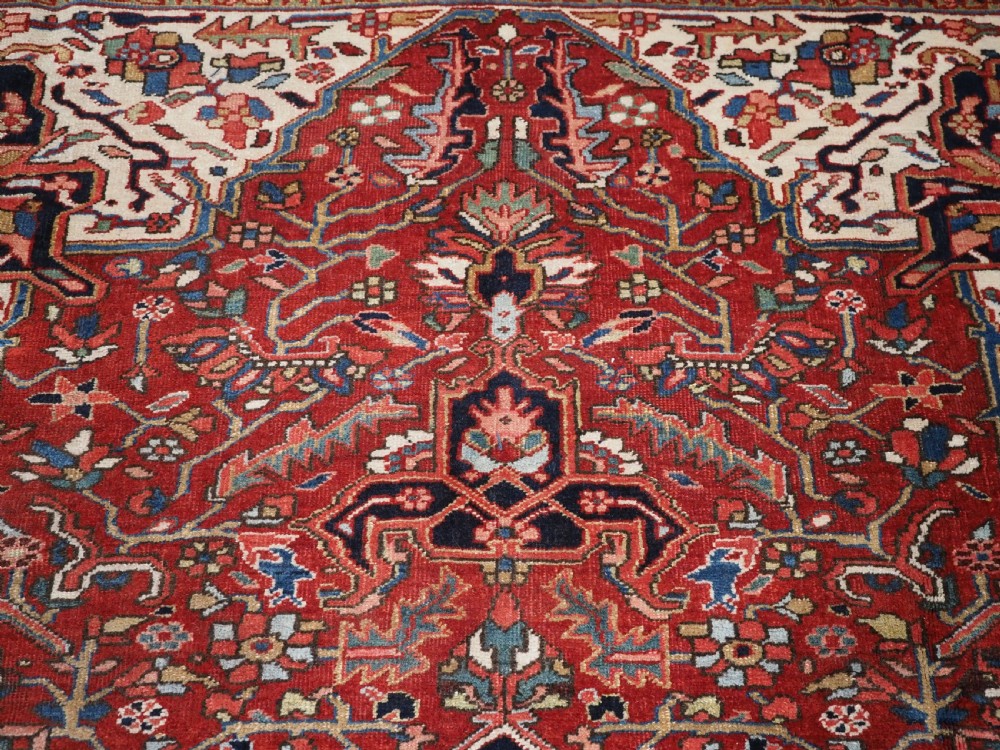 An antique hand-knotted Persian Heriz rug featuring a large geometric central medallion in navy blue, set upon a red field with off-white corner spandrels and a wide decorative border. View XI