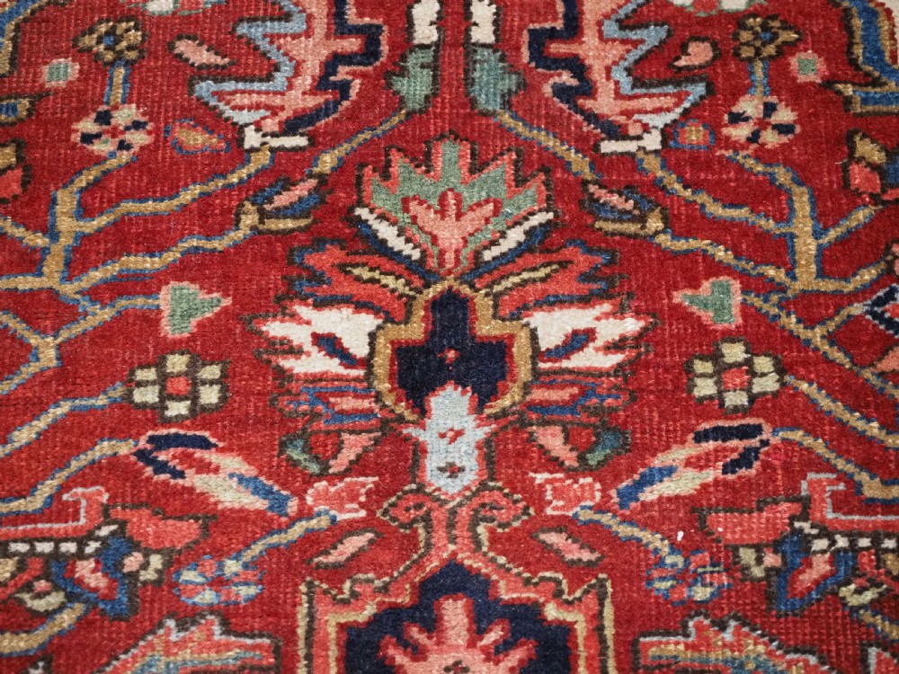 An antique hand-knotted Persian Heriz rug featuring a large geometric central medallion in navy blue, set upon a red field with off-white corner spandrels and a wide decorative border. View XII