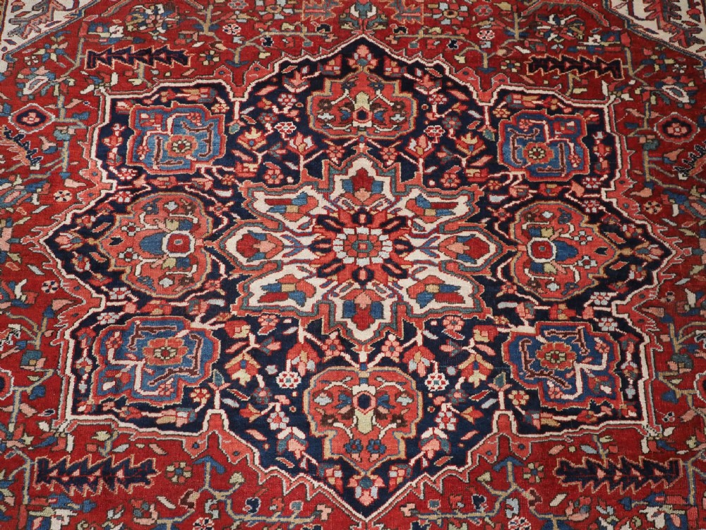 An antique hand-knotted Persian Heriz rug featuring a large geometric central medallion in navy blue, set upon a red field with off-white corner spandrels and a wide decorative border. View XIII