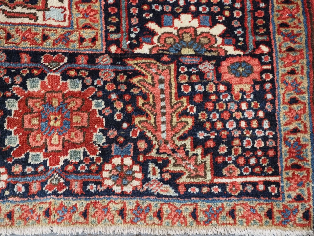 An antique hand-knotted Persian Heriz rug featuring a large geometric central medallion in navy blue, set upon a red field with off-white corner spandrels and a wide decorative border. View XIV