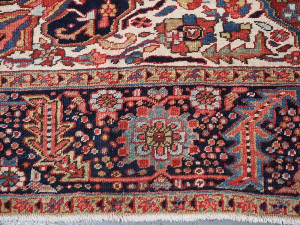 An antique hand-knotted Persian Heriz rug featuring a large geometric central medallion in navy blue, set upon a red field with off-white corner spandrels and a wide decorative border. View XV