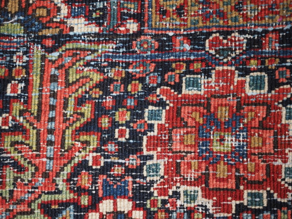 An antique hand-knotted Persian Heriz rug featuring a large geometric central medallion in navy blue, set upon a red field with off-white corner spandrels and a wide decorative border. View XVI