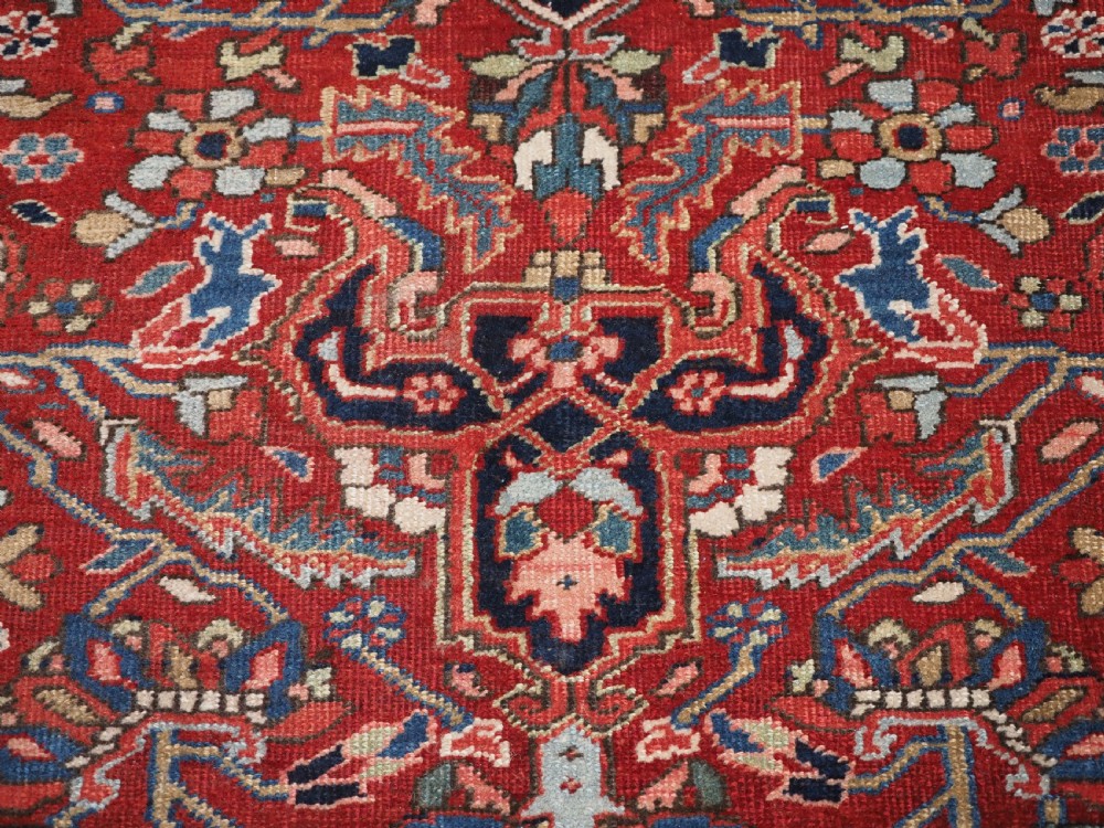 An antique hand-knotted Persian Heriz rug featuring a large geometric central medallion in navy blue, set upon a red field with off-white corner spandrels and a wide decorative border. View XVIII