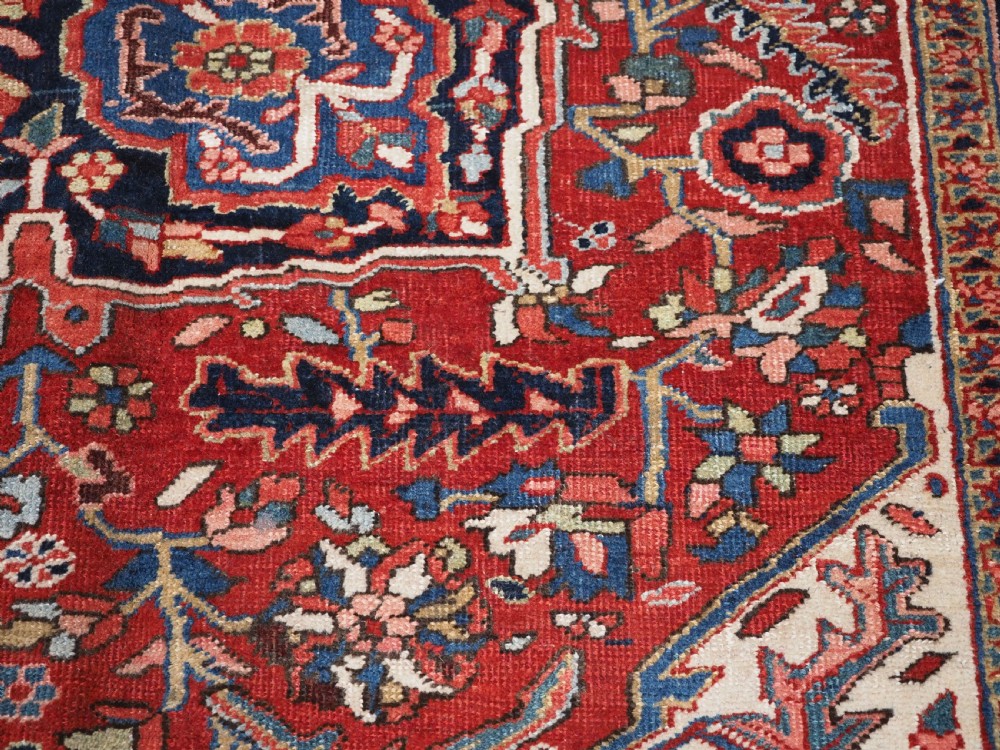 An antique hand-knotted Persian Heriz rug featuring a large geometric central medallion in navy blue, set upon a red field with off-white corner spandrels and a wide decorative border. View XIX