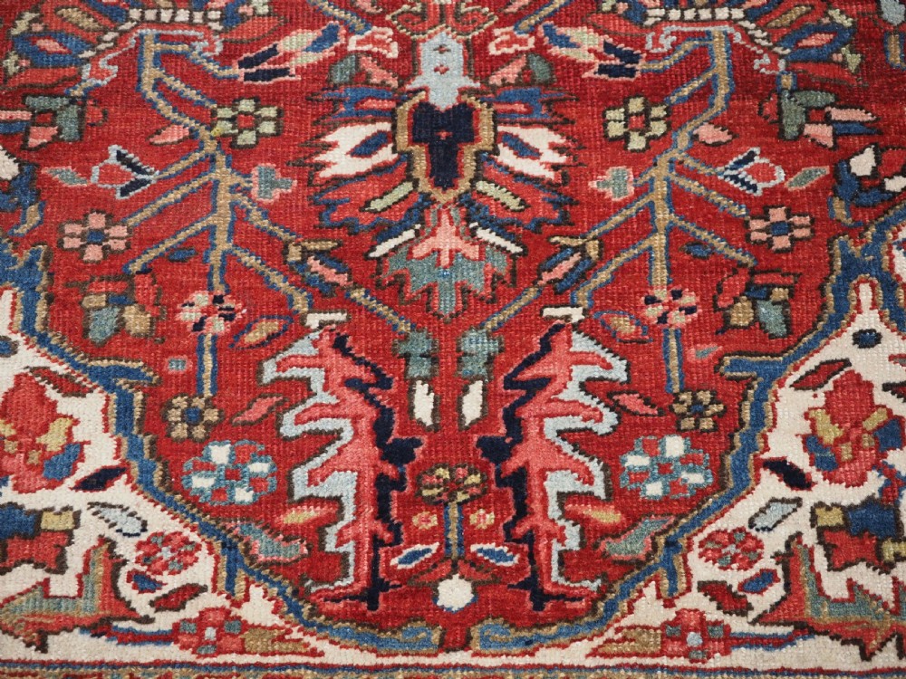 An antique hand-knotted Persian Heriz rug featuring a large geometric central medallion in navy blue, set upon a red field with off-white corner spandrels and a wide decorative border. View XX