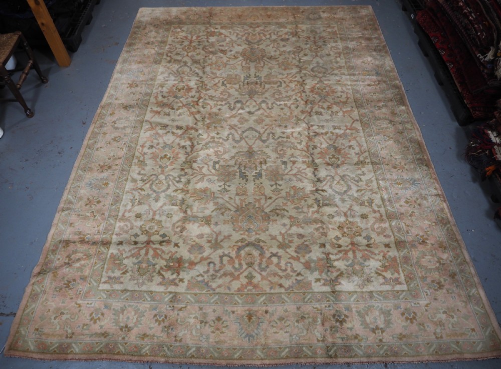 An antique Turkish Oushak wool carpet featuring a soft pink and beige ground decorated with pastel floral palmette patterns and multi-layered borders. View III