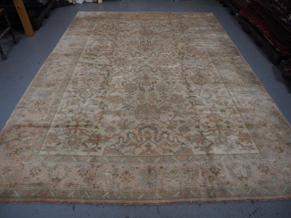 An antique Turkish Oushak wool carpet featuring a soft pink and beige ground decorated with pastel floral palmette patterns and multi-layered borders. View IV