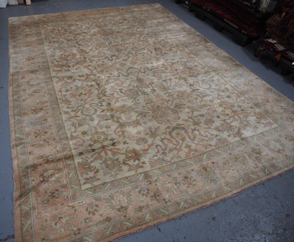 An antique Turkish Oushak wool carpet featuring a soft pink and beige ground decorated with pastel floral palmette patterns and multi-layered borders. View V