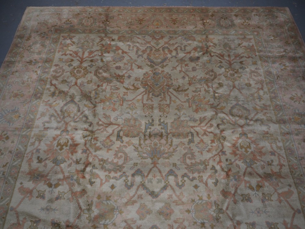 An antique Turkish Oushak wool carpet featuring a soft pink and beige ground decorated with pastel floral palmette patterns and multi-layered borders. View VI
