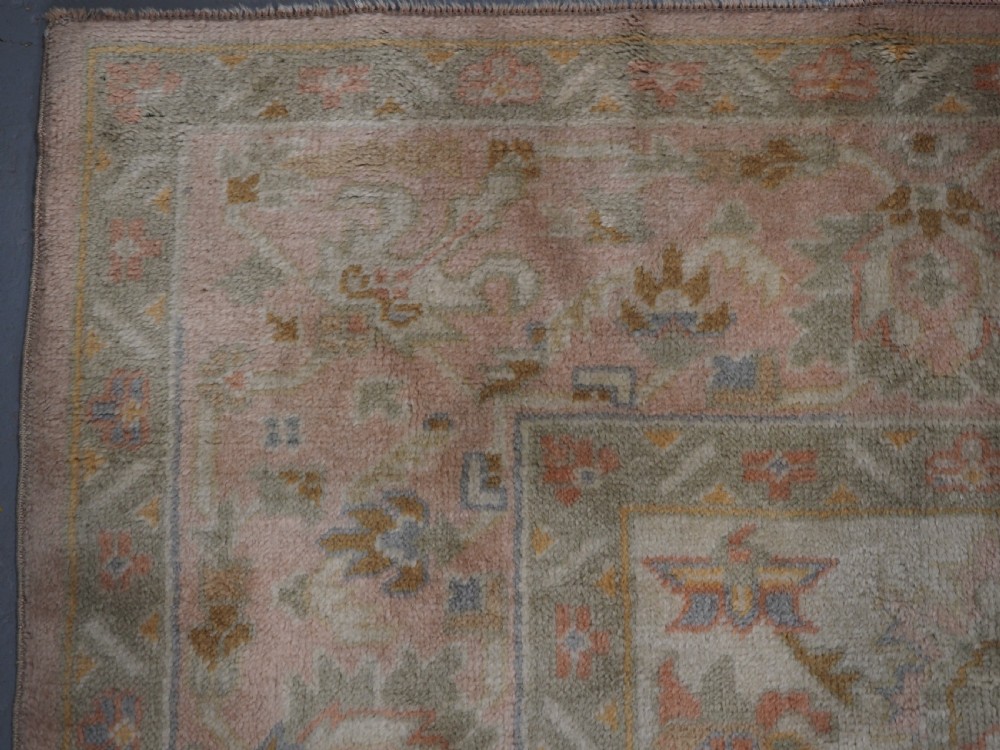 An antique Turkish Oushak wool carpet featuring a soft pink and beige ground decorated with pastel floral palmette patterns and multi-layered borders. View IX