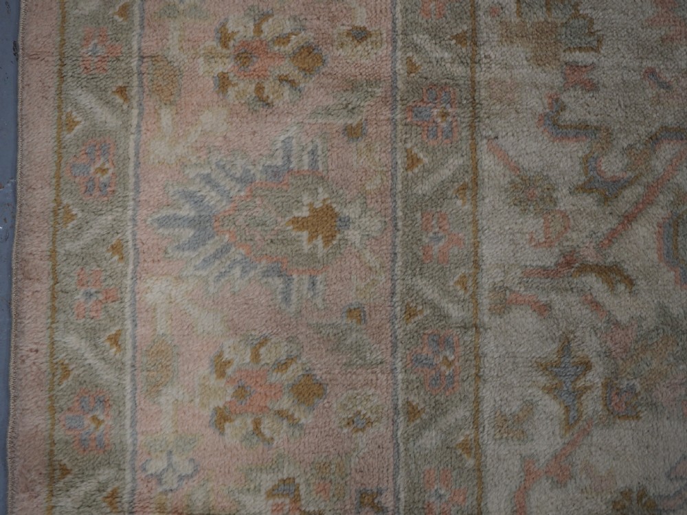 An antique Turkish Oushak wool carpet featuring a soft pink and beige ground decorated with pastel floral palmette patterns and multi-layered borders. View X