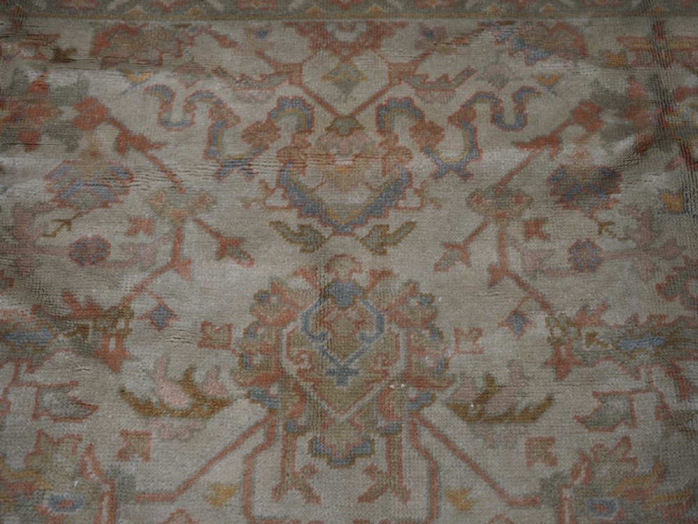 An antique Turkish Oushak wool carpet featuring a soft pink and beige ground decorated with pastel floral palmette patterns and multi-layered borders. View XI