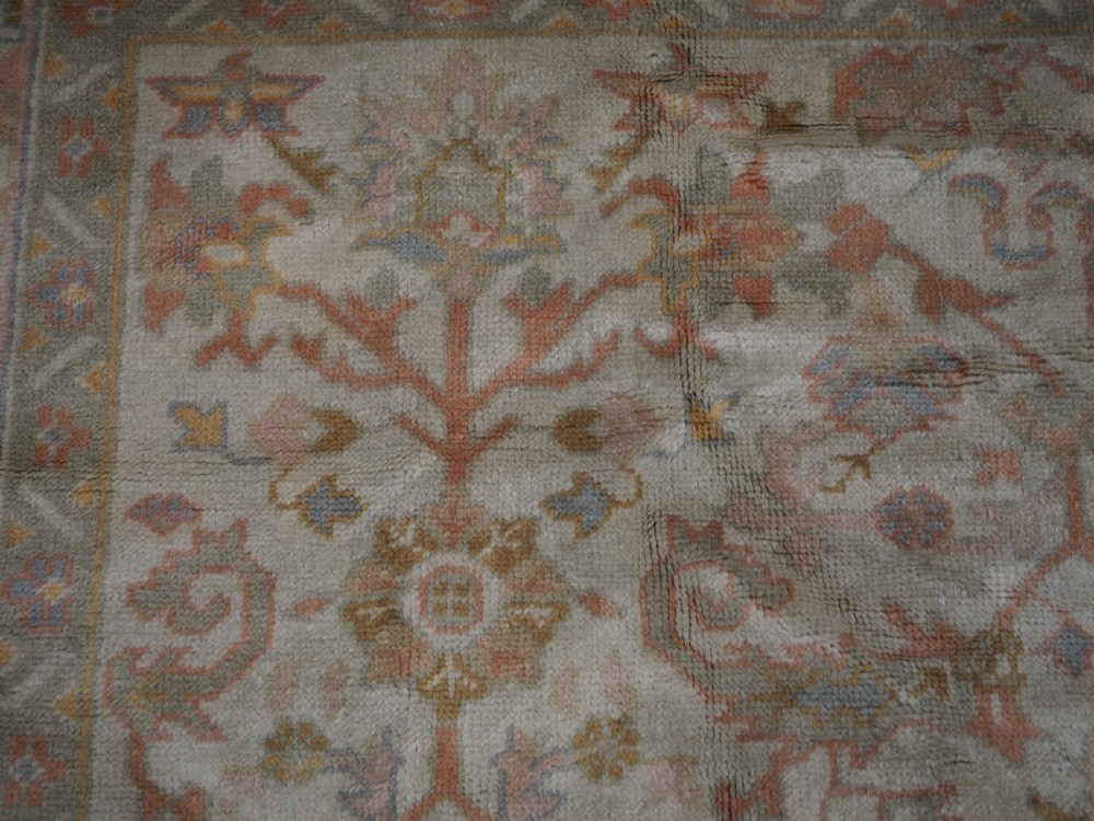 An antique Turkish Oushak wool carpet featuring a soft pink and beige ground decorated with pastel floral palmette patterns and multi-layered borders. View XII