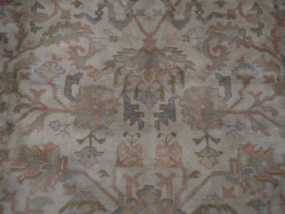 An antique Turkish Oushak wool carpet featuring a soft pink and beige ground decorated with pastel floral palmette patterns and multi-layered borders. View XIV