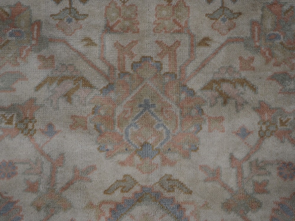 An antique Turkish Oushak wool carpet featuring a soft pink and beige ground decorated with pastel floral palmette patterns and multi-layered borders. View XV