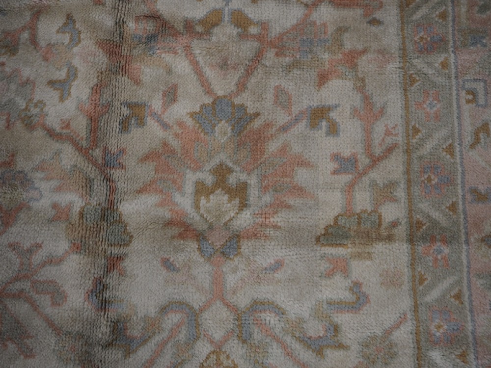 An antique Turkish Oushak wool carpet featuring a soft pink and beige ground decorated with pastel floral palmette patterns and multi-layered borders. View XVI