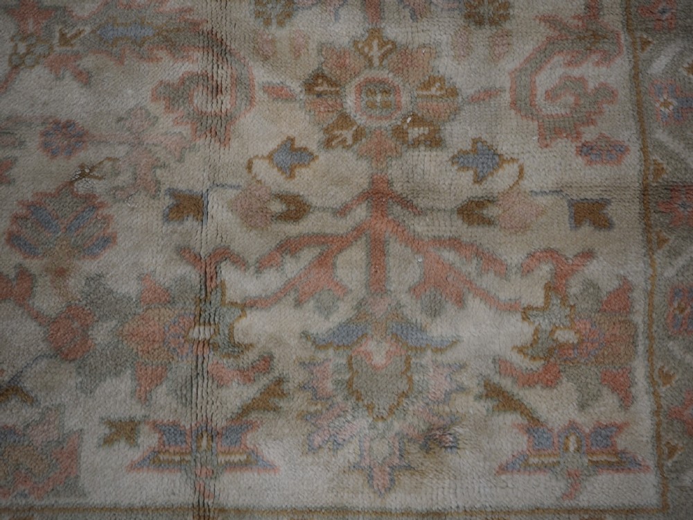 An antique Turkish Oushak wool carpet featuring a soft pink and beige ground decorated with pastel floral palmette patterns and multi-layered borders. View XVII