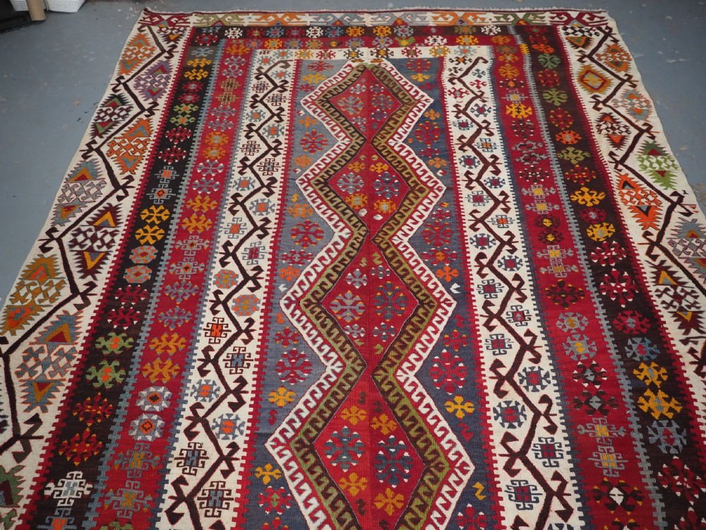 A large flatwoven antique Turkish Kayseri wool kilim rug featuring central red diamond medallions surrounded by geometric patterned borders. View V