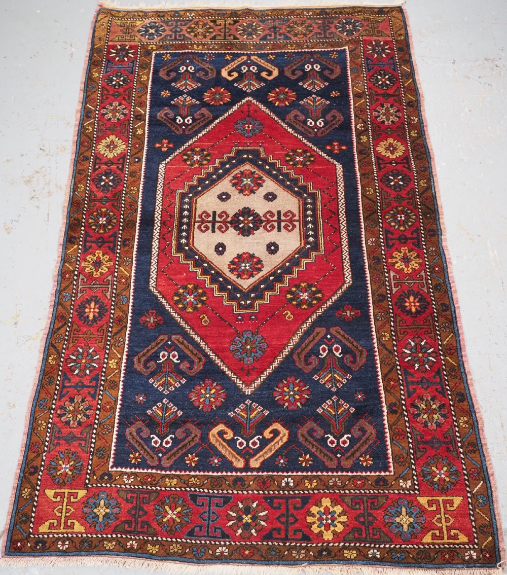 An antique hand-knotted Turkish Yahyali wool rug featuring a central geometric medallion design in red, cream, and navy blue with ornate floral borders.