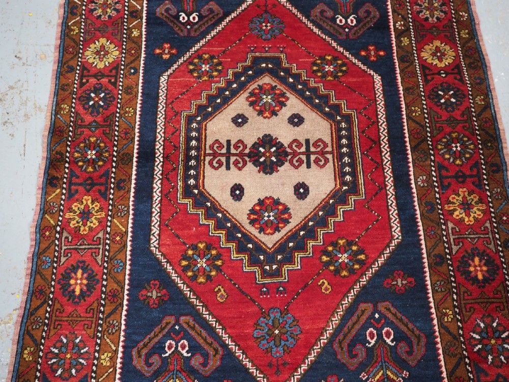 An antique hand-knotted Turkish Yahyali wool rug featuring a central geometric medallion design in red, cream, and navy blue with ornate floral borders. View IV