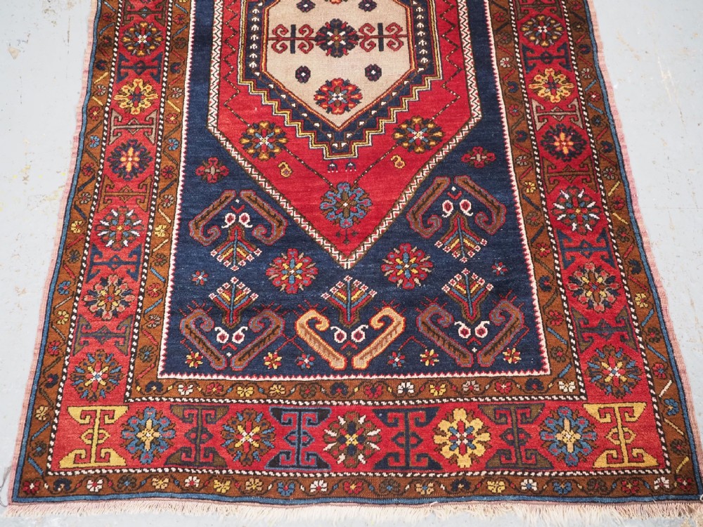 An antique hand-knotted Turkish Yahyali wool rug featuring a central geometric medallion design in red, cream, and navy blue with ornate floral borders. View V
