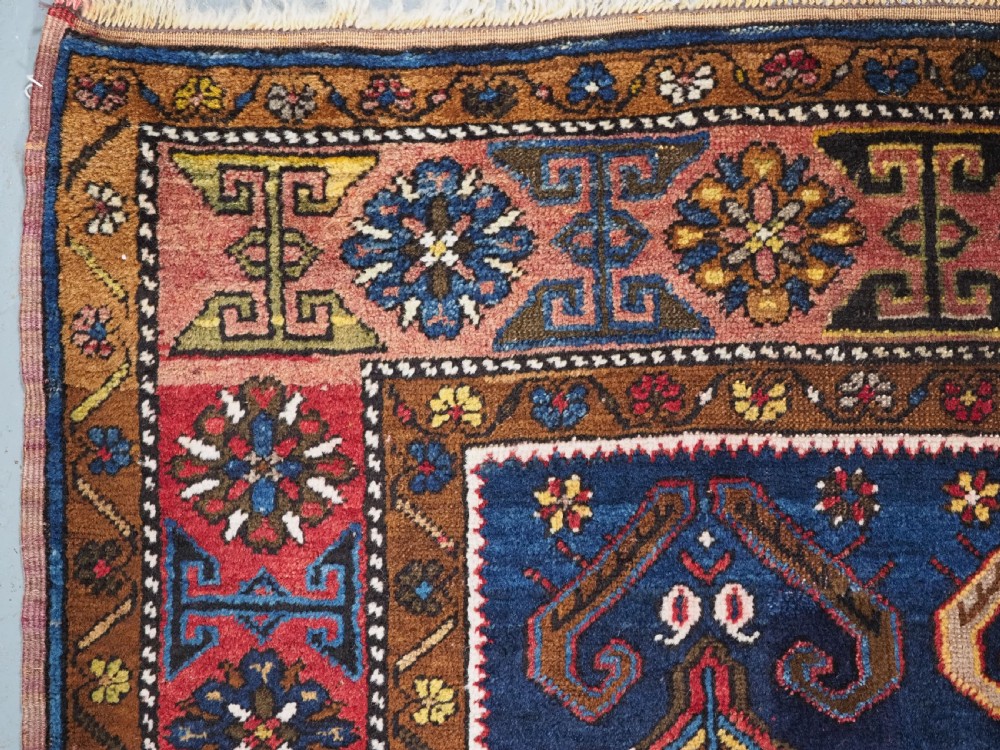 An antique hand-knotted Turkish Yahyali wool rug featuring a central geometric medallion design in red, cream, and navy blue with ornate floral borders. View VI
