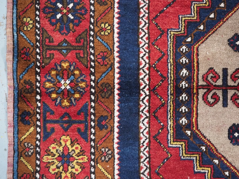 An antique hand-knotted Turkish Yahyali wool rug featuring a central geometric medallion design in red, cream, and navy blue with ornate floral borders. View VII