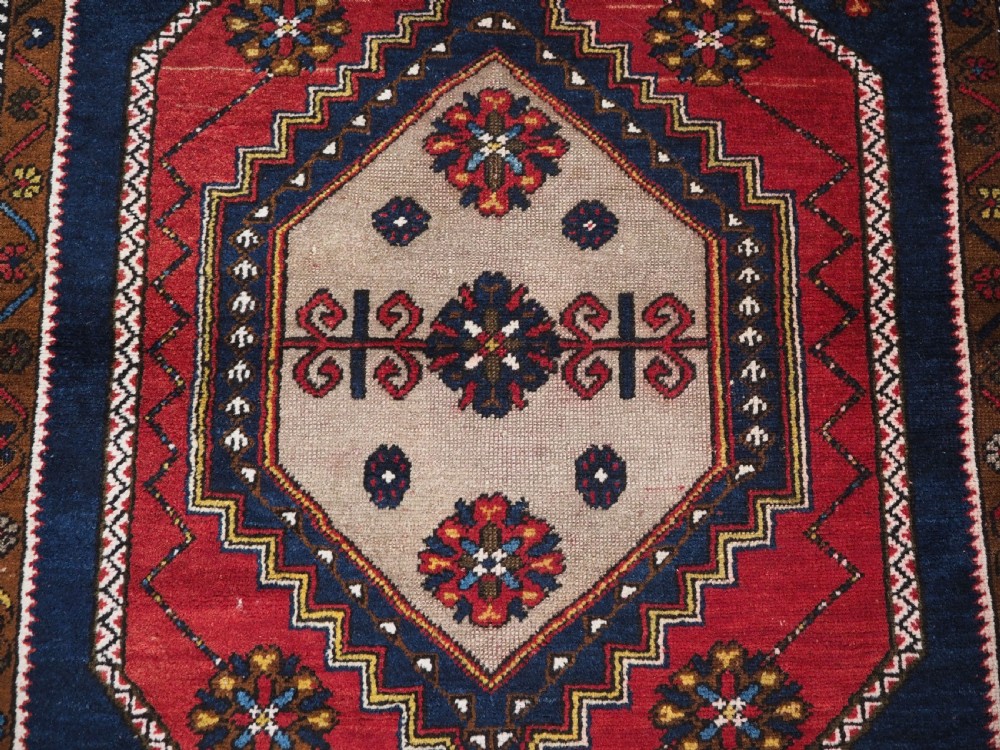 An antique hand-knotted Turkish Yahyali wool rug featuring a central geometric medallion design in red, cream, and navy blue with ornate floral borders. View IX