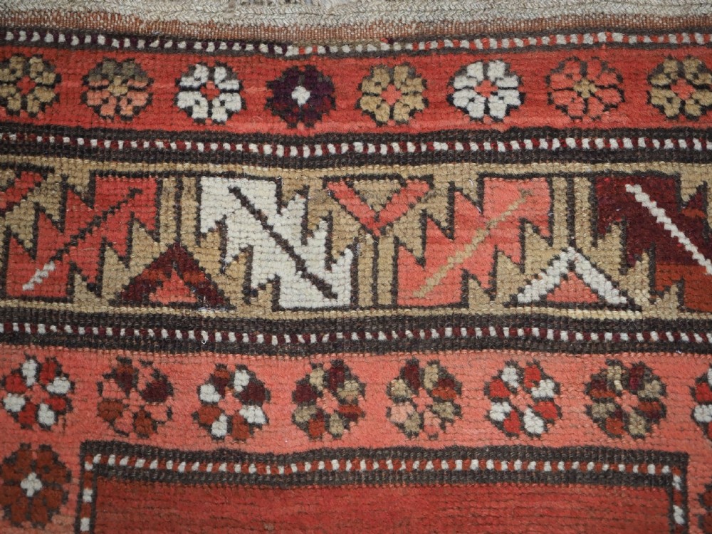 An antique hand-knotted wool rug featuring an unadorned terracotta red field framed by complex geometric and floral patterned borders. View VIII