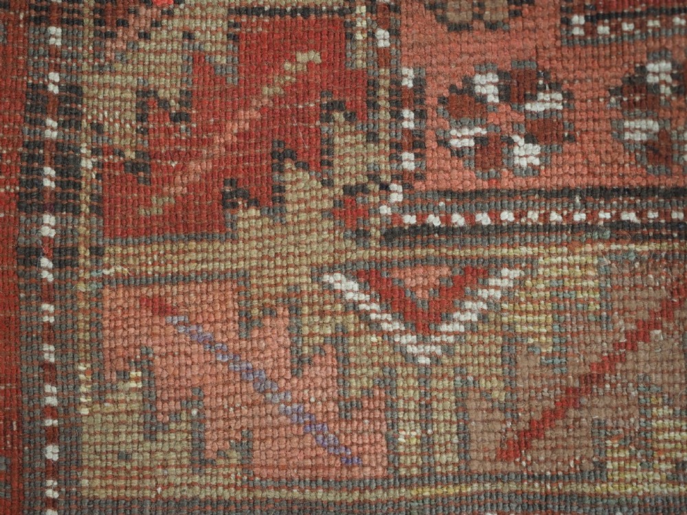 An antique hand-knotted wool rug featuring an unadorned terracotta red field framed by complex geometric and floral patterned borders. View XI