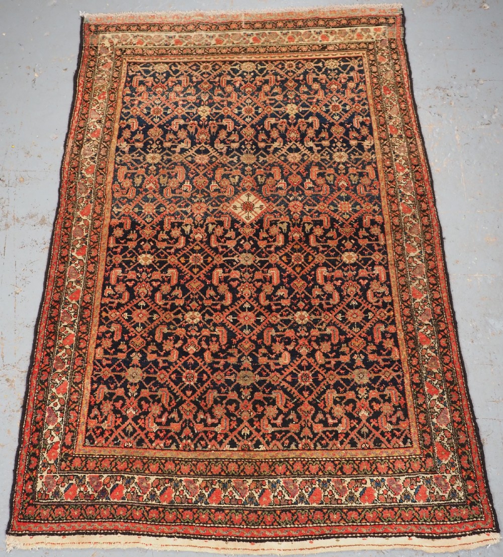 An antique Persian Malayer hand-knotted wool rug featuring an intricate all-over Herati lattice pattern on a dark navy blue field surrounded by multi-layered terracotta floral borders.
