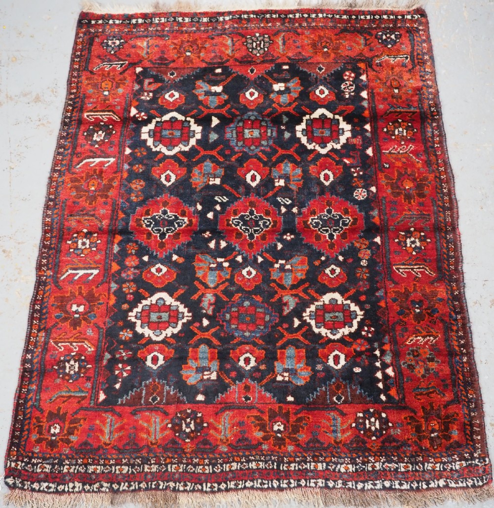 An antique hand-knotted Persian Shiraz wool rug featuring geometric tribal medallions in red, dark blue, and ivory.