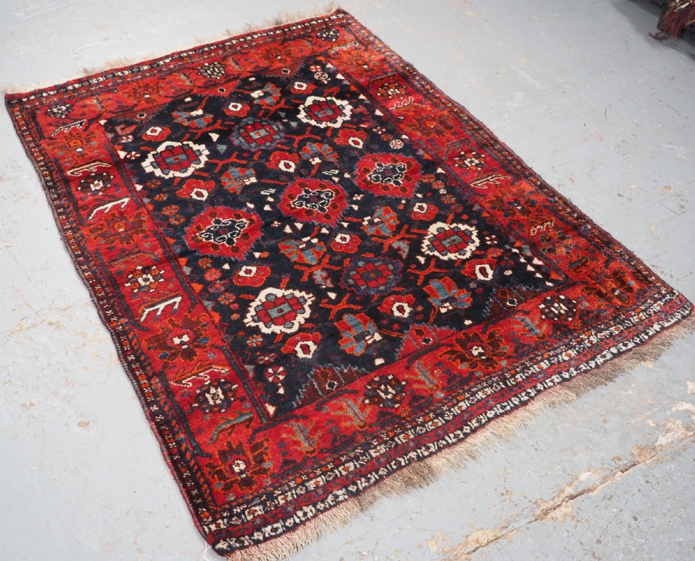 An antique hand-knotted Persian Shiraz wool rug featuring geometric tribal medallions in red, dark blue, and ivory. View II