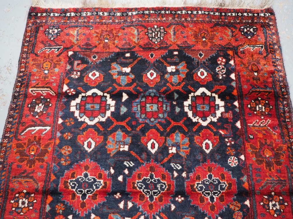 An antique hand-knotted Persian Shiraz wool rug featuring geometric tribal medallions in red, dark blue, and ivory. View III